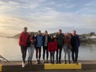 Group photo of IDCORE students standing a side of pier with sunset, sea and mountains in the background