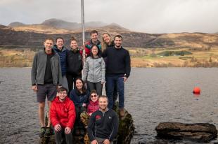 idocre students on a rock by a loch with mountains in the background