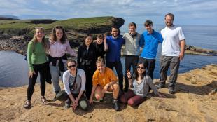 group photo of IDCORE students at the top of a cliff with sea and islands in the background